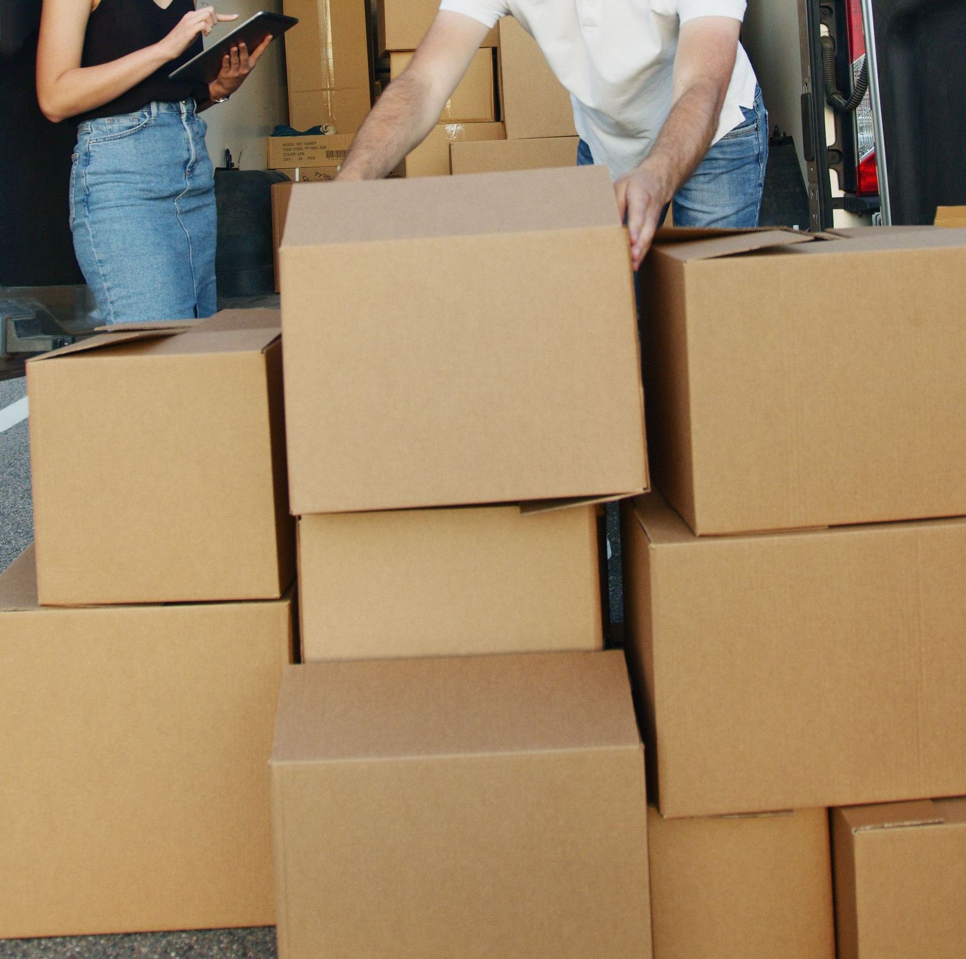 Two workers unloading cardboard boxes from a delivery van, teamwork and logistics concept.