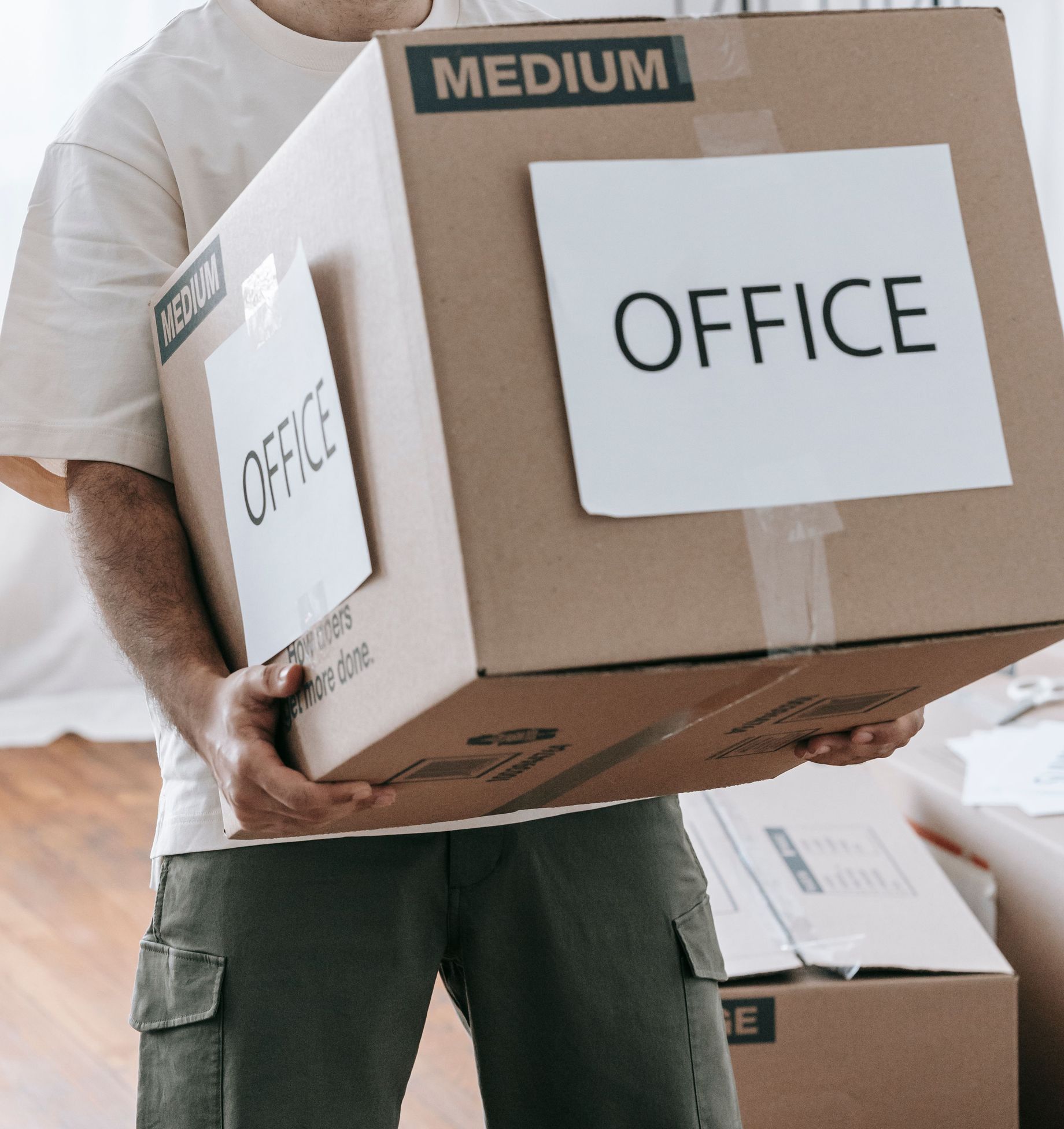 Man moving box labeled 'Office' indoors during relocation or packing.